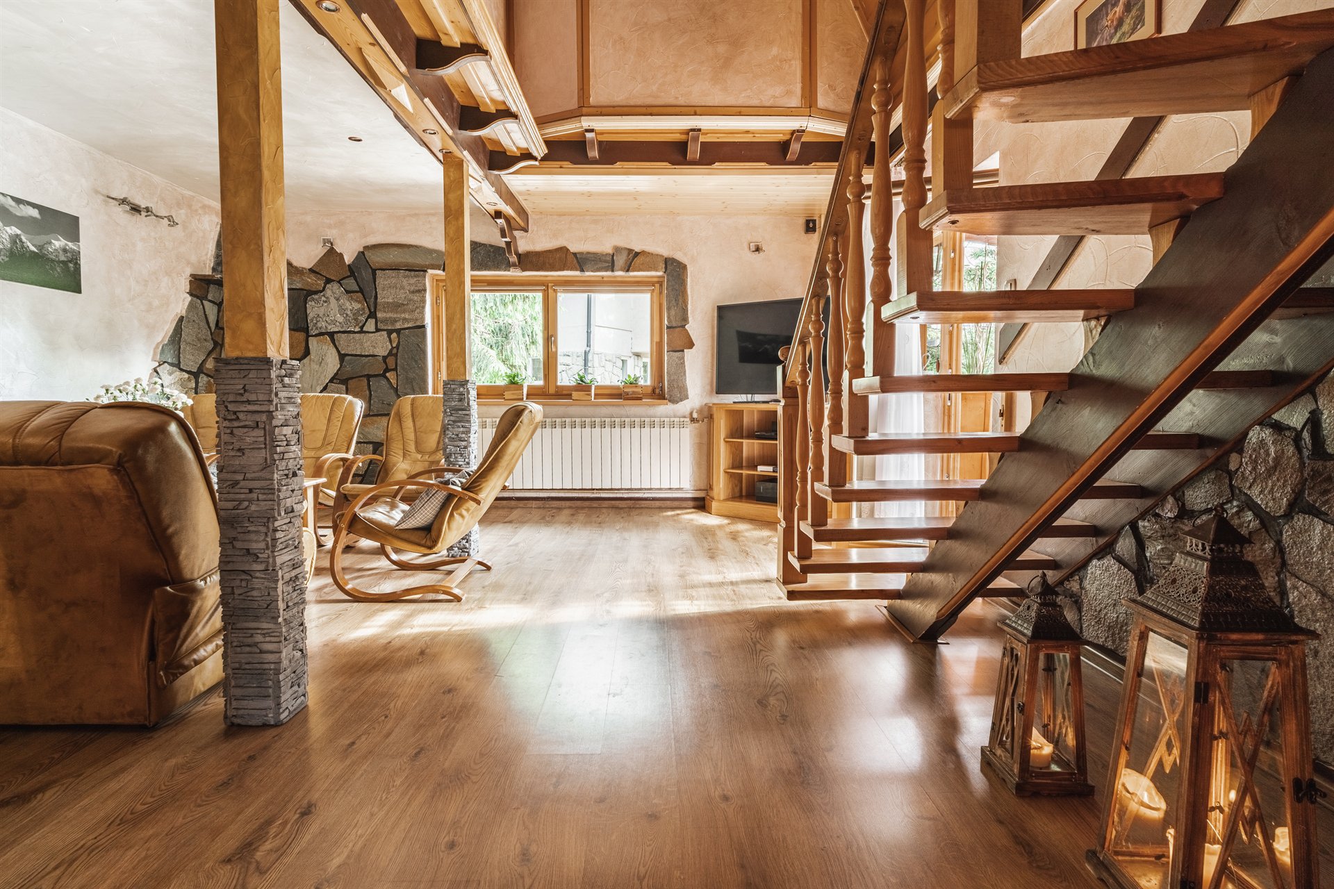 Przytulny salon w stylu rustykalnym z drewnianą antresolą i schodami, skórzane fotele i kamienna ściana