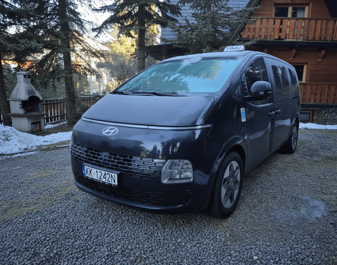 Ciemnoniebieski van Hyundai z taksówką na dachu zaparkowany na żwirowym podjeździe z tablicą KK1242N