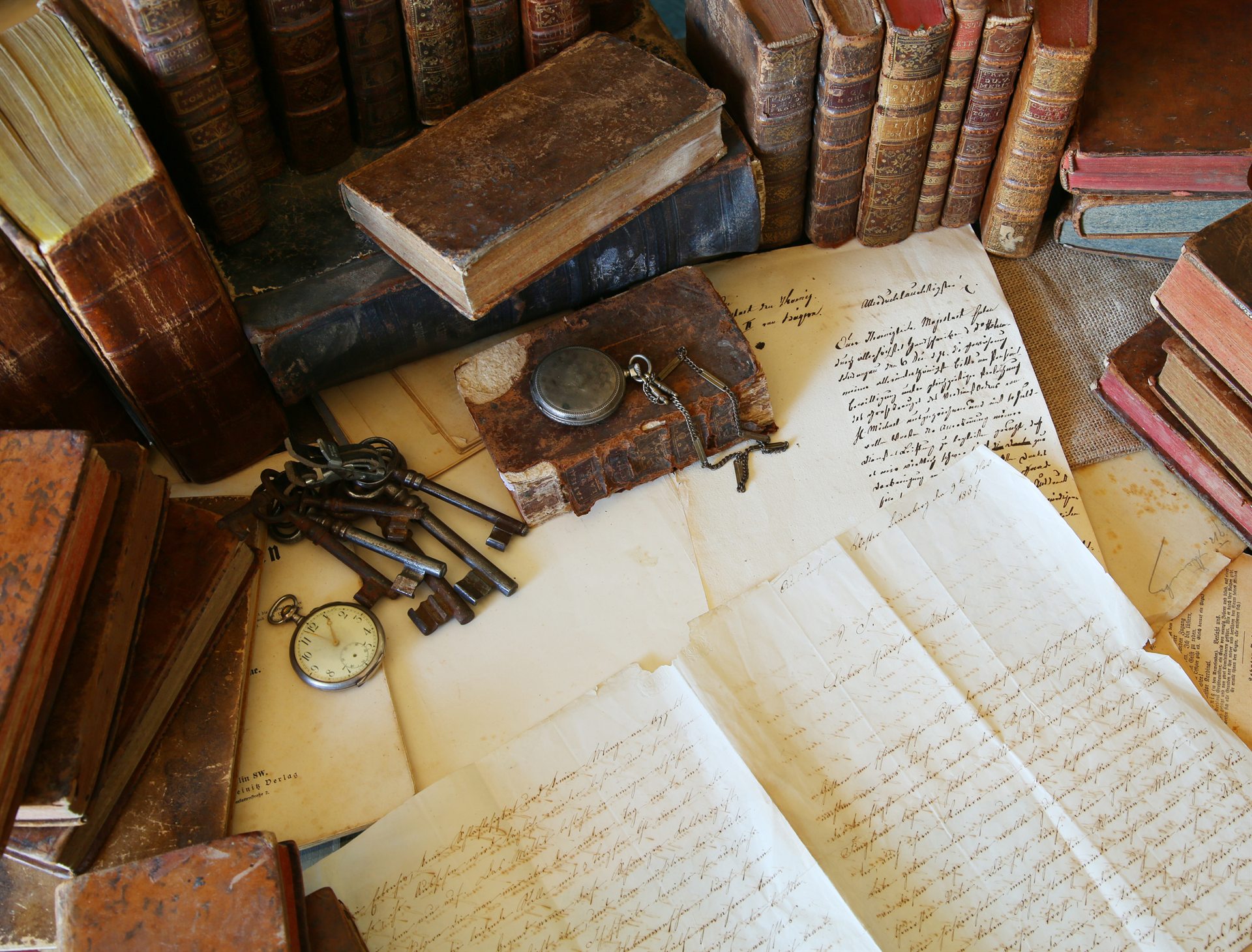 Stare skórzane księgi i pożółkłe listy na stole z zegarkiem kieszonkowym i pękiem starych metalowych kluczy